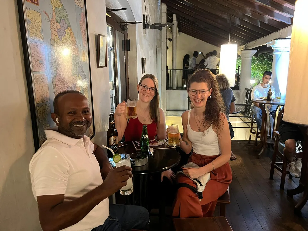 Tour guide Romesh celebrates with two female tour guests over a beer in a cozy bar in Sri Lanka.
